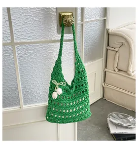 Detalle de bolso de hombro de punto verde calado con colgante de tulipán blanco.