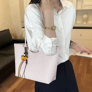 Detalle de bolso tote trenzado rosa llevado por una modelo en un ambiente interior