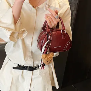Close-up view of a stylish dark red shiny bowling bag decorated with a plush bear charm.