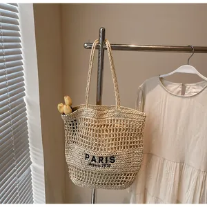 Vista detallada de un bolso tote de paja tejida con letras de PARIS en un perchero