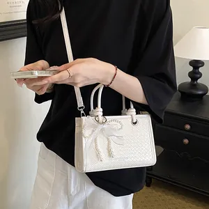 Elegante witte geweven handtas met parelstrikgalerie, ideaal voor zomerse uitstapjes.