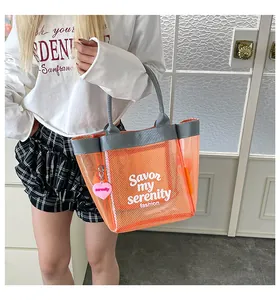 Detail view of the orange mesh transparent tote bag held by a model for a chic summer look
