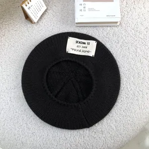 Detailed view of a soft black knitted beret hat featuring a vintage white cloth label
