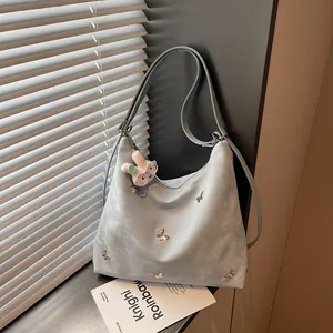 Detail view of large light blue suede hobo bag with butterfly accents and plush rabbit charm