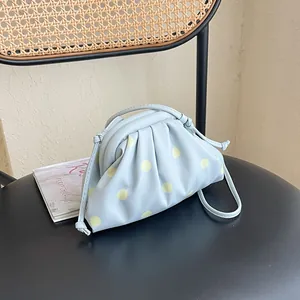Detailed view of light blue dumpling bag with yellow polka dots on a modern black chair.