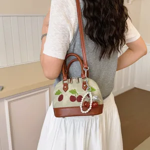 Vista detallada de un bolso bandolera beige con bordado de cerezas y llavero de perlas