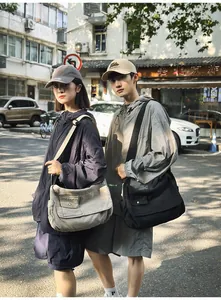Outdoor lifestyle shot showing two models wearing large solid color canvas messenger bags