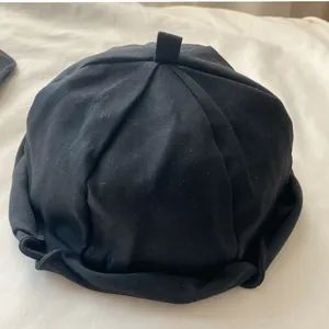 Detailed view of minimalist black pleated docker hat resting on soft white textured fabric