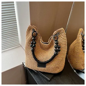 Close-up of a woven straw bucket bag with black beaded handles on a table.
