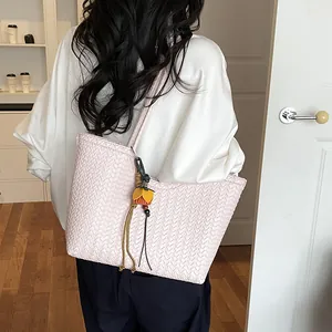 Vista detallada del elegante bolso tote tejido rosa claro con un colgante de borla