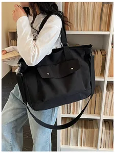 Model carrying a large black travel tote bag in a library setting with books.