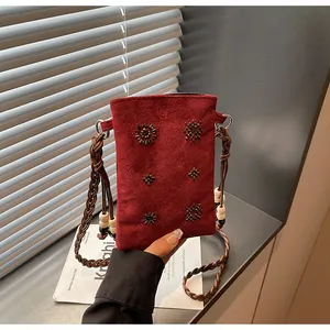 Detail of red suede crossbody phone bag with beaded flowers and braided leather strap.