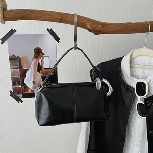 Glossy black vintage pillow handbag with silver chain detail hanging on a wooden branch