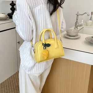 Model carrying a bright yellow pillow bag with a woven pineapple charm in a cafe