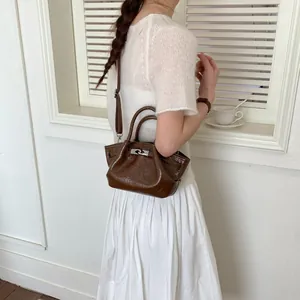 Vista laterale dettagliata di una mini borsa a secchiello marrone lucida su una modella