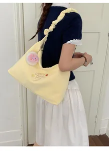 Detalle de un bolso hobo amarillo pálido con correa fruncida y dije de conejo en una modelo.