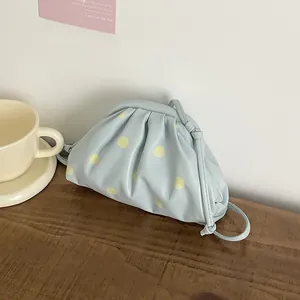 Detailed view of a light blue minimalist cloud bag with yellow polka dots on a wooden table