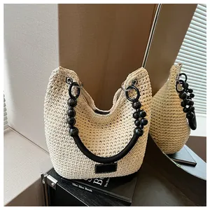 Detailed shot of a woven cream bucket bag with black beaded handle on a book