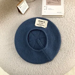Detail shot of a blue knitted beret with a stylish white letter patch and knit texture.
