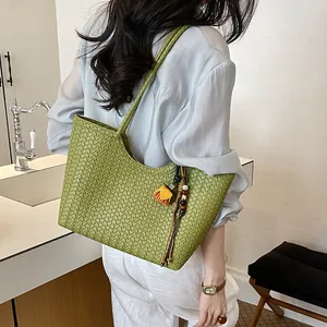 Primer plano de un bolso tote verde trenzado con un colgante floral, llevado por una modelo