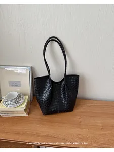 Detailed view of black woven tote bag on a wooden desk with lifestyle props