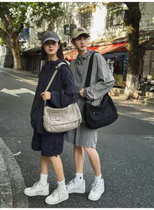 Detailed street style view of large minimalist canvas messenger bags on models outdoors.