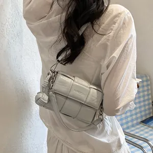 Close-up of a minimalist gray woven leather shoulder bag with decorative knot detail.