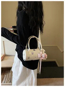 Model carrying a trendy cream barrel bag with cartoon prints and a pink bow charm.