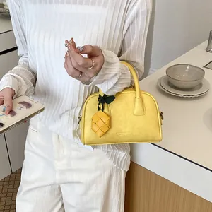 Detail view of stylish yellow pillow handbag with decorative woven charm accessory