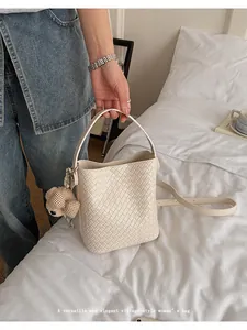 Woven bucket bag for women shown in a clean lifestyle setting on a white bed