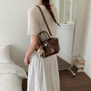 Elegante borsa a secchiello marrone lucida con orsetto su modella in bianco