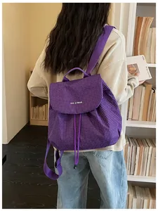 Back view of a trendy purple checkered mini backpack worn by a model in a library setting.