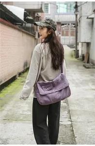 On-body view of a large purple canvas messenger bag worn by a model in a casual alley