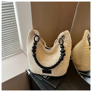 Detail view of a cream crochet bucket bag with a stylish black beaded handle on a table.