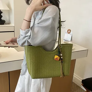 Detalle de un elegante bolso de hombro tejido en color verde llevado por una modelo
