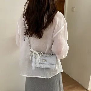 Detailed view of a stylish light blue quilted crossbody bag with decorative pearl and lace bow