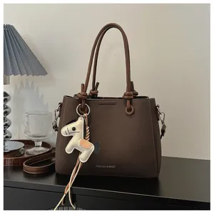 Detailed view of a brown pebbled leather bucket bag featuring a cute white horse charm