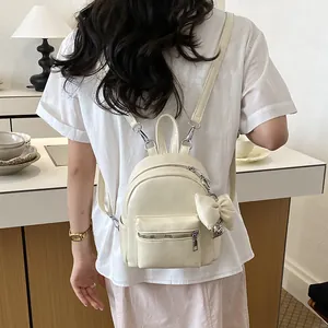 Mini-Rucksack aus cremeweißem Kunstleder mit Schleifenanhänger, getragen von einem Modell.