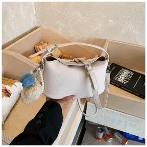 Cream white textured leather bucket bag with cute plush charm and adjustable strap.