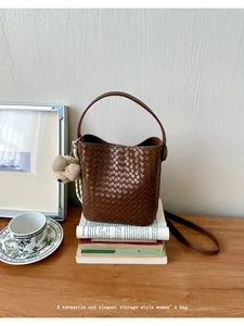 Elegant brown woven bucket bag with teddy bear charm displayed on a vintage wooden desk