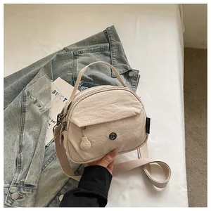 Vista detallada del bolso bandolera de nailon beige con cremalleras y textura de tela