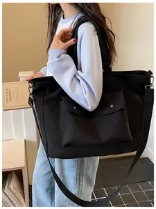Detail of a large black canvas tote bag being carried by a model in a casual setting.