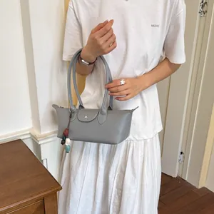 Élégant sac à bandoulière gris minimaliste tenu par un mannequin dans un cadre intérieur.