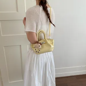 Vista posteriore donna in abito bianco con borsa a secchiello gialla e charm orso