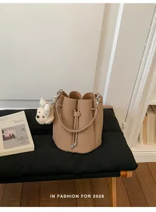 Detail view of a beige pebbled leather bucket bag with a cute plush dog charm on a bench
