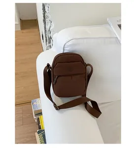 Close-up detail of a minimalist brown nylon crossbody mobile phone bag on a sofa