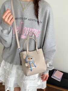 Minimalist beige lychee grain leather bucket bag with cute bear pendant for daily commute