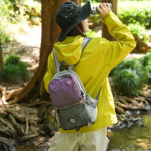 Frau mit Fernglas trägt einen leichten wasserfesten Wanderrucksack in der Natur