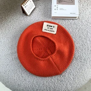 Detail view of orange knit beret with SEASON 13 letter patch on fuzzy background.