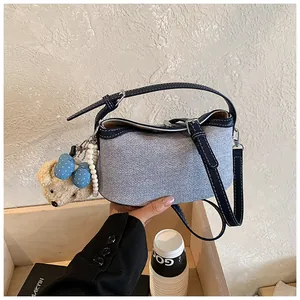 Close-up detail of a stylish denim bucket bag featuring a teddy bear charm and pearl strap